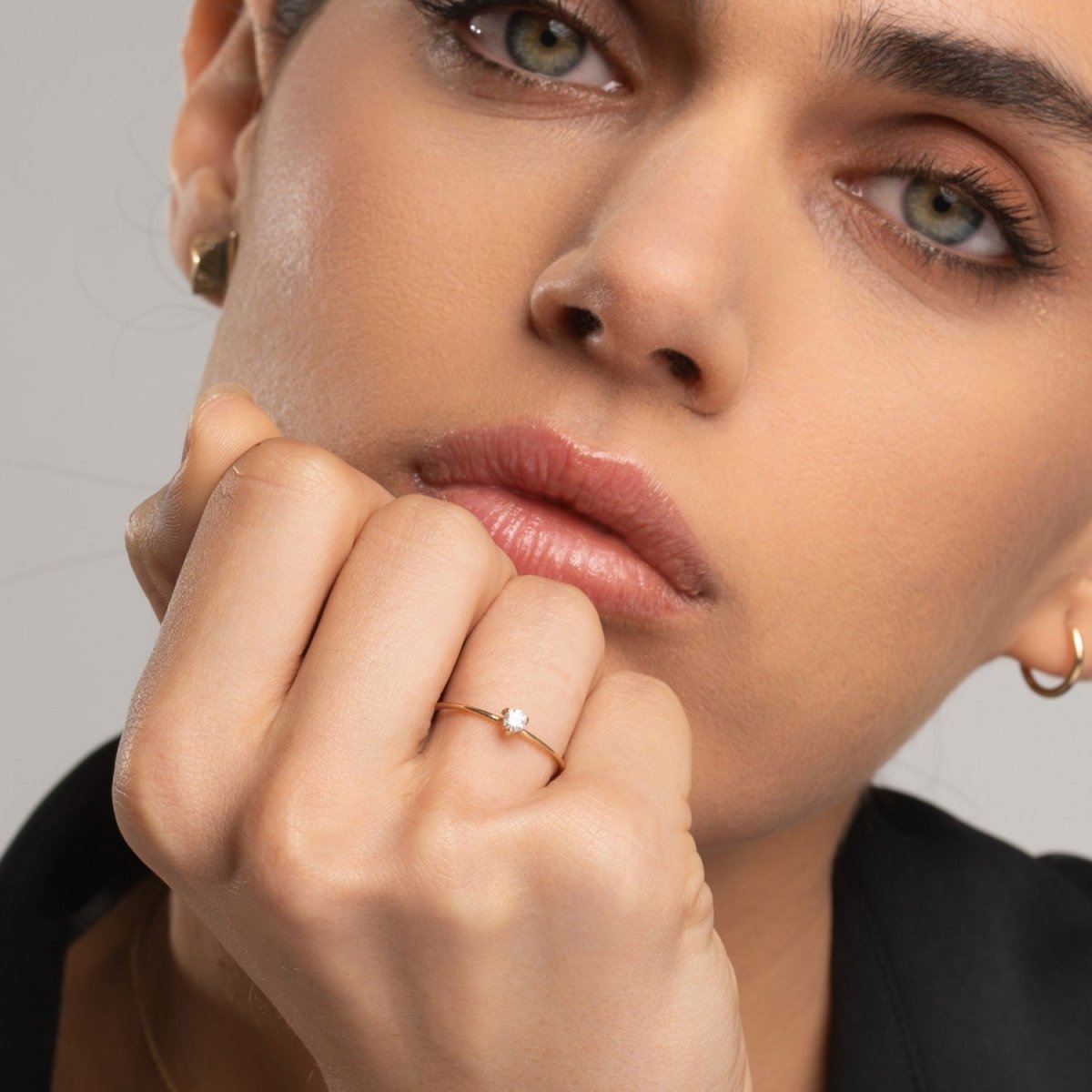 Woman wearing a dainty 14k yellow gold solitaire diamond ring, styled with gold earrings. The round-cut diamond catches the light, adding a subtle sparkle.