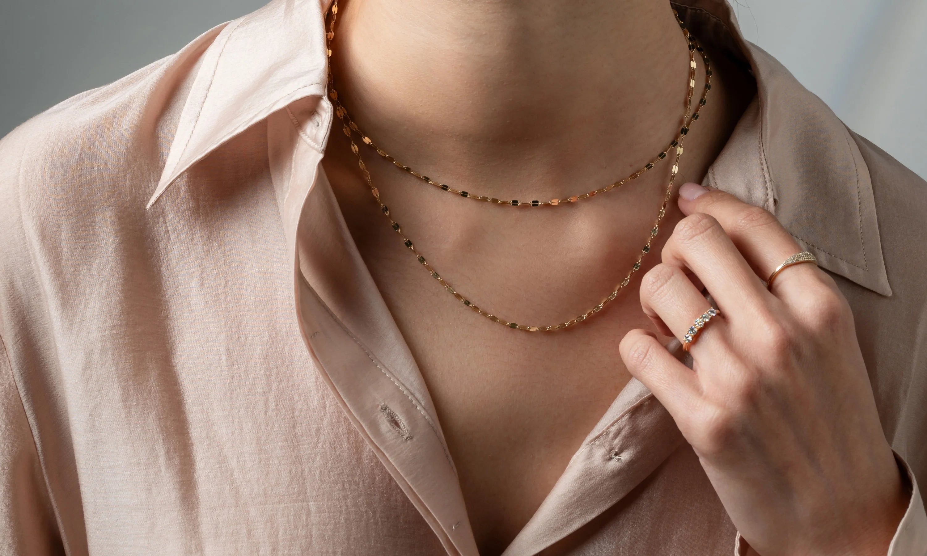 Woman wearing layered 14k gold necklaces and elegant diamond rings, styled with a soft beige blouse, showcasing timeless Mother's Day gifts.