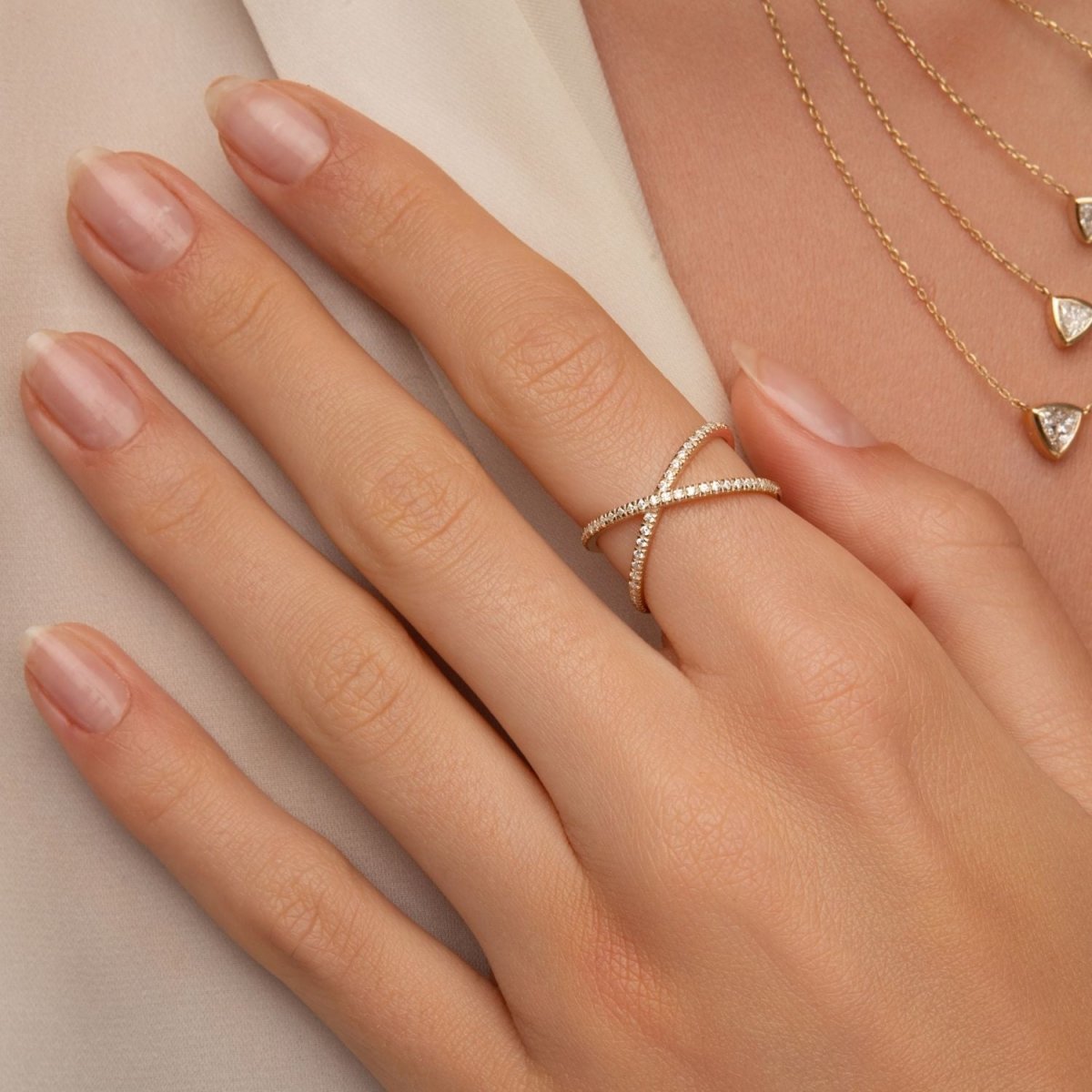 A close-up of a woman’s hand wearing a 14k yellow gold diamond X crossover ring, capturing the intricate crisscross diamond design and sleek gold finish.
