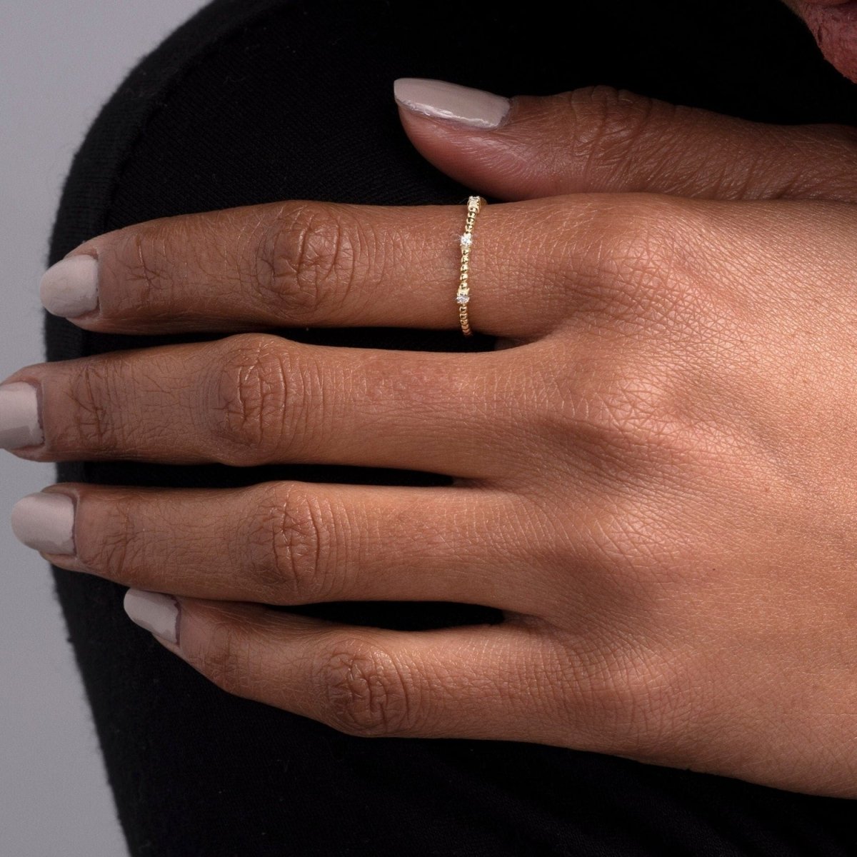 A woman’s hand adorned with a 14k yellow gold diamond beaded ring, showcasing its delicate gold spheres and three shimmering round diamonds. A refined and timeless accessory.